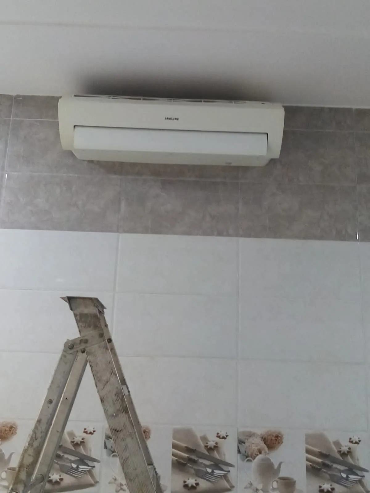 مكيف سبليت فوق جدار مبلط وسلم وأدوات على الأرض